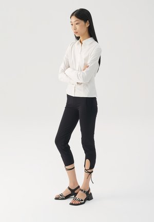 Bela dolga srajca z dolgimi rokavi, zapeta in s ovratnikom; kombinirana s črnimi skrajšanimi hlačami z izrezi in trdilnimi trakovi. Črne sandale z zebra vzorcem.