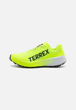 Zapatilla de correr en amarillo neón con parte superior de malla, branding negro "TERREX" y una entresuela blanca contorneada. Cuenta con una suela exterior negra rugosa para mayor tracción.