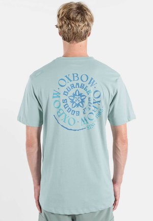 T-shirt en coton bleu clair avec un grand motif circulaire au dos, composé de texte et de motifs dans des nuances de bleu plus foncé. Manches courtes, coupe décontractée.