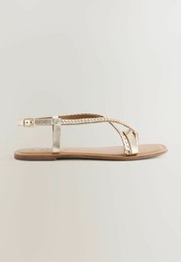 Gouden platte sandalen met gevlochten banden, een smalle enkelband met een gesp en een gladde bruine zool. Minimalistisch ontwerp met een elegante afwerking.