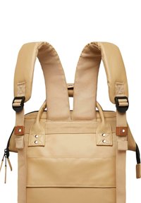 Zaino color tan con spallacci imbottiti, corpo in tessuto testurizzato, dettagli in pelle e accessori in metallo per resistenza e supporto.