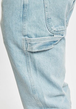 Hellblaue Denim-Hosen verfügen über eine Seitentasche mit Klappe, kontrastierenden Nähten und eine lockere Passform, die einen strukturierten Stoff zur Geltung bringt.