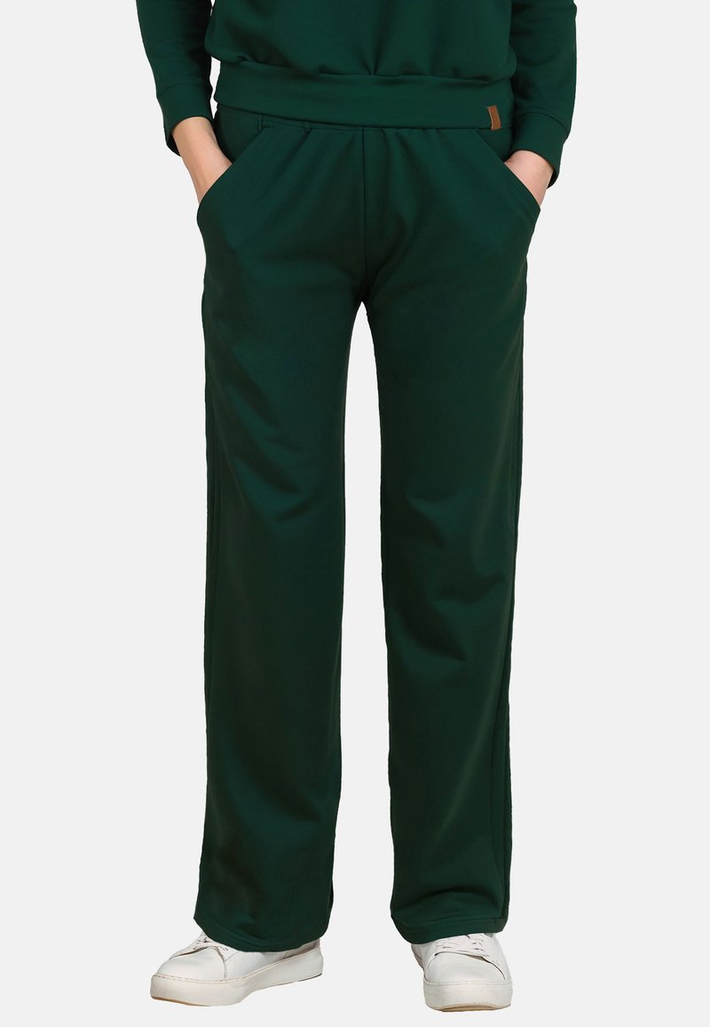 Donkergroene, wijde broek van zachte stof met een elastische tailleband en zijzakken, gecombineerd met witte schoenen.