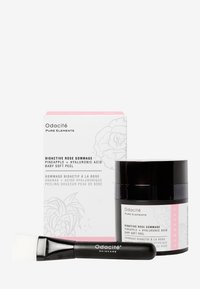 Le set Odacité Bioactive Rose Gommage comprend un pot noir avec une étiquette rose, un emballage blanc avec un design floral et un applicateur en brosse noir.
