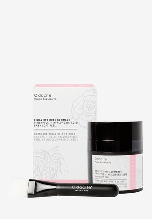 Odacité Bioactive Rose Gommage-settet inkluderer en svart krukke med en rosa etikett, hvit emballasje med blomstermønster, og en svart penselapplicator.