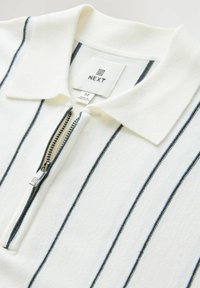White pullover with blue vertical stripes, zippered collar, and soft textured fabric. Features a “NEXT” brand label and medium size tag.