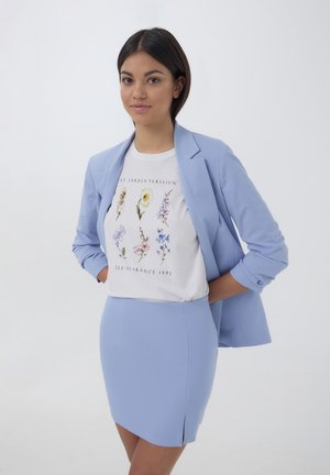 Blazer blu chiaro sopra una t-shirt bianca con stampa floreale; gonna mini blu chiaro abbinata con uno spacco laterale, texture liscia.