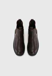 Botas de tobillo de cuero marrón con una textura suave, paneles laterales elásticos y suela de goma negra. Presentan tiradores en la parte trasera para facilitar su uso.