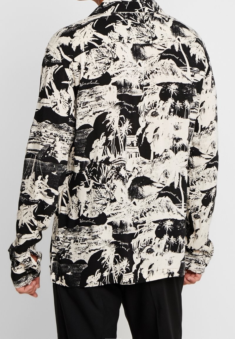 Schwarz-weißes Langarmhemd mit einem markanten, abstrakten tropischen Muster aus Palmen und Landschaften; lockerer Sitz und Knopfmanschetten.