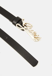 Ceinture en cuir noir avec une boucle en métal doré en forme du mot "Guess", présentant une texture lisse et un design classique.