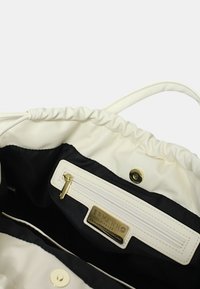 Interno di borsa in pelle bianca con rivestimento in tessuto nero, dotato di una tasca con zip e componenti in oro, incluso un etichetta del marchio.