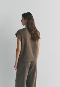 Lyhythihainen ruskea paita, jossa rento istuvuus ja pehmeää kangasta. Siinä on pyöreä pääntie ja hienovaraiset ompelu- ja yksityiskohdat, yhditettynä samaan sävyyn sopivien housujen kanssa.