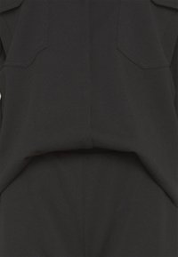 Czarna odzież o strukturalnym wzorze, z dwiema kieszeniami na piersi, gładką fakturą oraz złożonym fragmentem w talii.