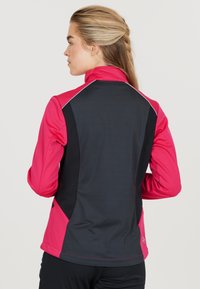 Fittet atletisk jakke med en pink front og sort ryg, høj krave, kontrasterende syninger og sidelommer.