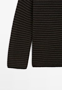 Primo piano di un tessuto lavorato a maglia a strisce orizzontali nera e marrone scuro, che mostra parte di una manica e del corpo di un indumento.