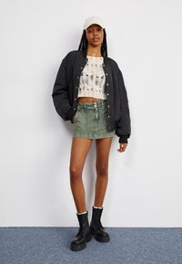 Mustapomberitakki, valkoinen virkatut crop-top, oliivinvihreä farkkuhame ja mustat nauhakengät. Neutraali lippalakki viimeistelee asun.
