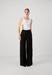 Bílé tílko s malým černým logem, doplněné širokými černými cargo kalhotami s bočními kapsami. Oblečení doplňuje žlutá kabelka přes rameno.