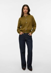 Sweter-krótka kardigan w oliwkowej zieleni z srebrnymi guzikami, zestawiony z ciemnoniebieskimi dżinsami o prostych nogawkach, prezentowany na modelce. Czysty design i dopasowanie.