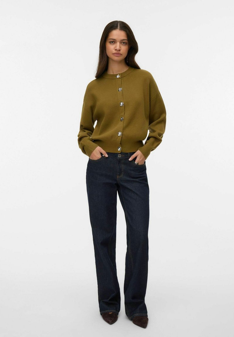 Sweter-krótka kardigan w oliwkowej zieleni z srebrnymi guzikami, zestawiony z ciemnoniebieskimi dżinsami o prostych nogawkach, prezentowany na modelce. Czysty design i dopasowanie.