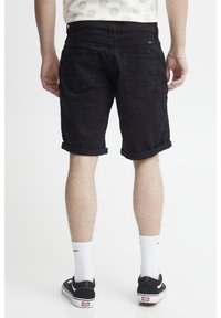Svarte denim shorts med optrukkede kanter, der har to baglommer. Båret med sorte slip-on sko og hvide sportsstrømper.