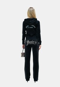 Črn velur trenerka, ki vključuje kapuco in hlače. Kapuca ima bele napise; hlače prikazujejo "Juicy" v bleščeči podrobnosti. Majhna torbica z vzorcem leopardjega kožuha.