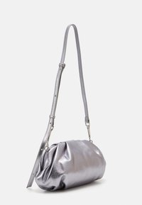 Metalisk sølvfarvet håndtaske med en rund form, guillet tekstur og en enkelt justerbar rem. Har en skinnende, glat lædermateriale.