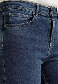 Granatowe dżinsy o dopasowanym kroju, z kontrastującymi żółtymi przeszyciami, pięcioma kieszeniami i zapięciem na zamek błyskawiczny.