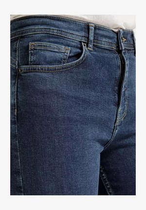 Granatowe dżinsy o dopasowanym kroju, z kontrastującymi żółtymi przeszyciami, pięcioma kieszeniami i zapięciem na zamek błyskawiczny.