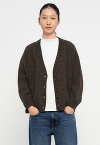 Temno rjav oversize kardigan iz teksturirane pletenine, ki ima V-izrez, rebraste manšete in pet velikih gumbov spredaj.