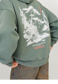 Vihreä huppari, jossa valkoinen maisemakuva takana ja punaiset tekstikoristeet. Resoriset hihansuut ja helma.