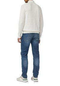 Weißer Pullover mit langen Ärmeln und Kragen, kombiniert mit blauen Jeans aus Denim. Die Schuhe sind hell mit grünen Akzenten. Einfarbiger, strukturierter Stoff.