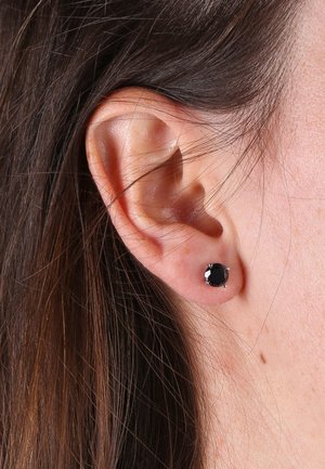 Boucle d'oreille noire en forme ronde, montée sur un support en métal argenté. La boucle d'oreille présente une pierre taillée avec une finition brillante.