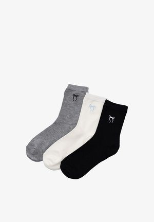 Trzy skarpety sięgające połowy łydki w kolorach szarym, białym i czarnym, każda z małym haftowanym wzorem kokardki w pobliżu mankietu.