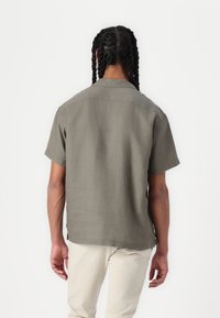 Camicia a maniche corte con colletto in tessuto verde oliva dalla texture liscia. Presenta un orlo dritto e spacchi laterali per il comfort.