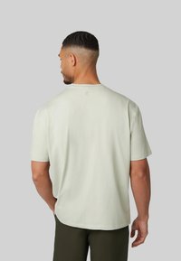 Lichtgroene katoenen T-shirt met een ronde hals, korte mouwen en een subtiele logodetail op de achterkant. Zachte textuur, relaxed fit.