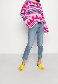 Rosa och mångfärgad mönstrad tröja med långa ärmar, kombinerad med ljusblå raka jeans och gula öppen-tå-skor.