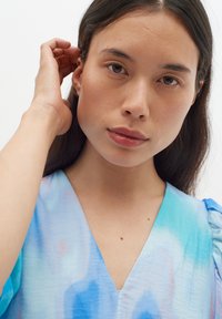 V-hals, blouse met korte mouwen in gradient tinten van blauw en zachtroze. Lichtgewicht stof met een gladde textuur en een subtiel patroon.