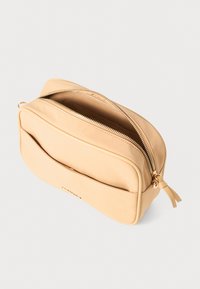Beige kompakt rektangulær taske med guld lynlås delvist åben og flad forlommt lomme, sat op mod en ensfarvet hvid baggrund.