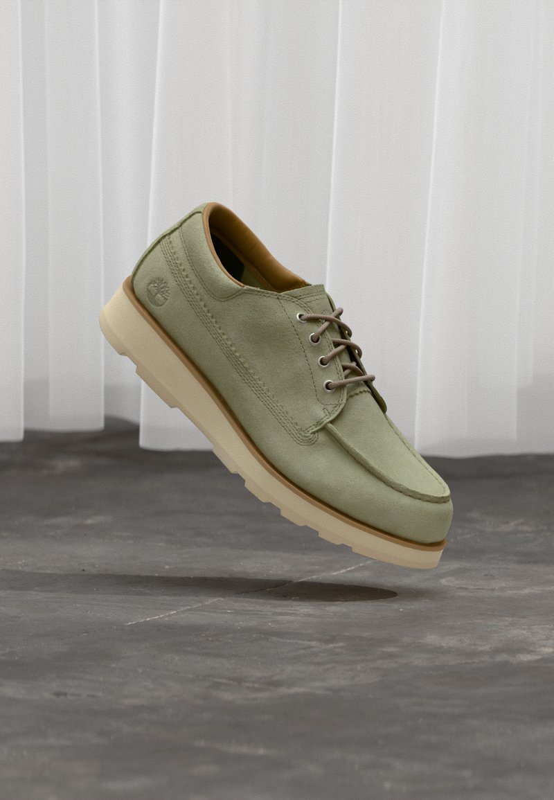 Πράσινο παπούτσι από καστόρι με ομαλή υφή, στρογγυλεμένη μύτη και καφέ κορδόνια. Διαθέτει παχύ, κρεμ χρώματος πάτο και λογότυπο στο πλάι.