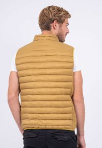 Gilet rembourré beige avec un matelassage horizontal et un col montant, fabriqué en matériau léger. Il dispose d'une fermeture éclair et d'un ourlet contrasté.