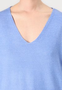 Pull en maille bleu clair avec un design à col en V. Le tissu semble doux et texturé, avec un style décontracté et léger.