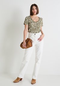 Camisa de manga corta verde oliva con patrón de hojas blancas, combinada con jeans blancos de tiro alto, bolso de ante marrón y botines beige.