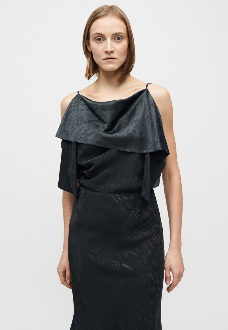 Abito nero con strato superiore drappeggiato leggermente lucido, caratterizzato da texture con motivi sottili. Design aderente con spalline regolabili.