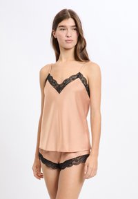 Satynowy zestaw do spania w miękkim brzoskwiniowym kolorze z czarną koronkową lamówką na topie i szortach. Regulowane ramiączka i gładka tekstura zwiększają komfort.