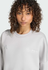 Sweat-shirt gris clair à col rond, avec logo adidas embossé et marquage Mercedes AMG Petronas. Texture douce avec une coupe décontractée.