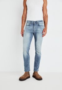 Jeans de denim azul claro con un ajuste slim, que cuentan con bolsillos frontales y un acabado desgastado; combinados con botas de tobillo de ante marrón.