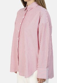 Camisa de botones a rayas rojas y blancas con cuello, de corte holgado, mangas anchas y dobladillo curvado. Textura de tela de algodón.