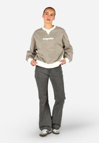 Csíkos, oversize szürke pulóver fehér bordázott mandzsettákkal és szegéllyel, fehér logó szöveggel. Flare szürke farmernadrággal és sportcipővel párosítva.