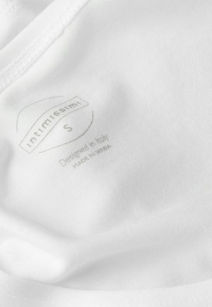 Hvidt stof, der viser et plejelabel med teksten "Intimissimi S Designet i Italien Fremstillet i Serbien" i lys gråtryk. Glat tekstur.