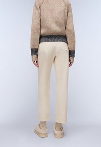 Beige knitted sweater with a textured finish and blue accents, paired with cream-colored trousers and cozy beige footwear.